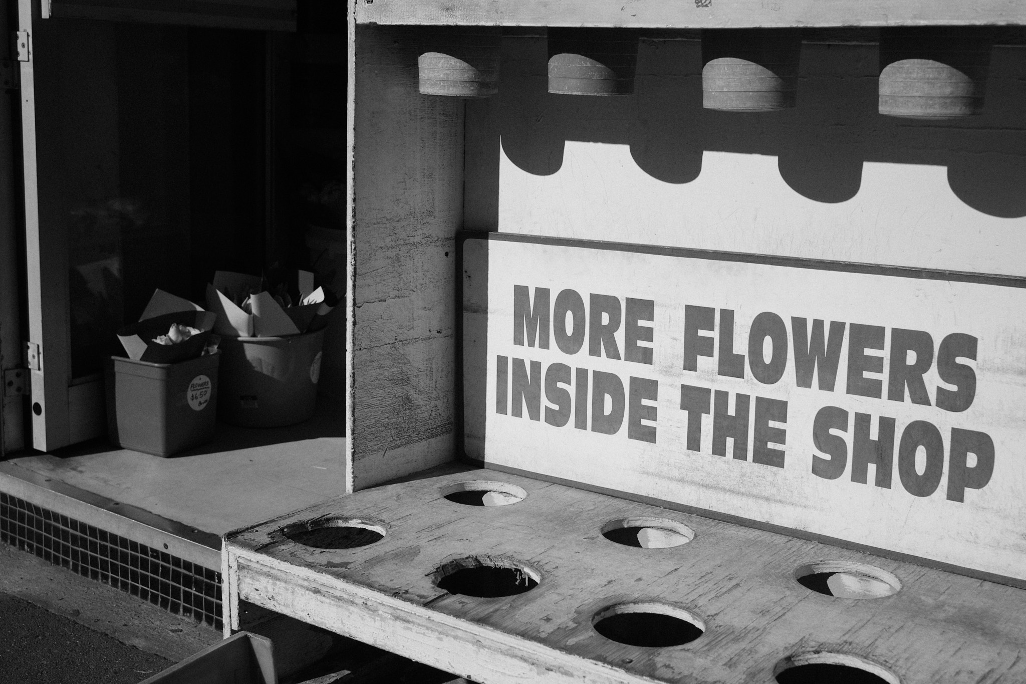 A sign reads 'More Flowers Inside the Shop' with a view of flowers peaking out of the doorway