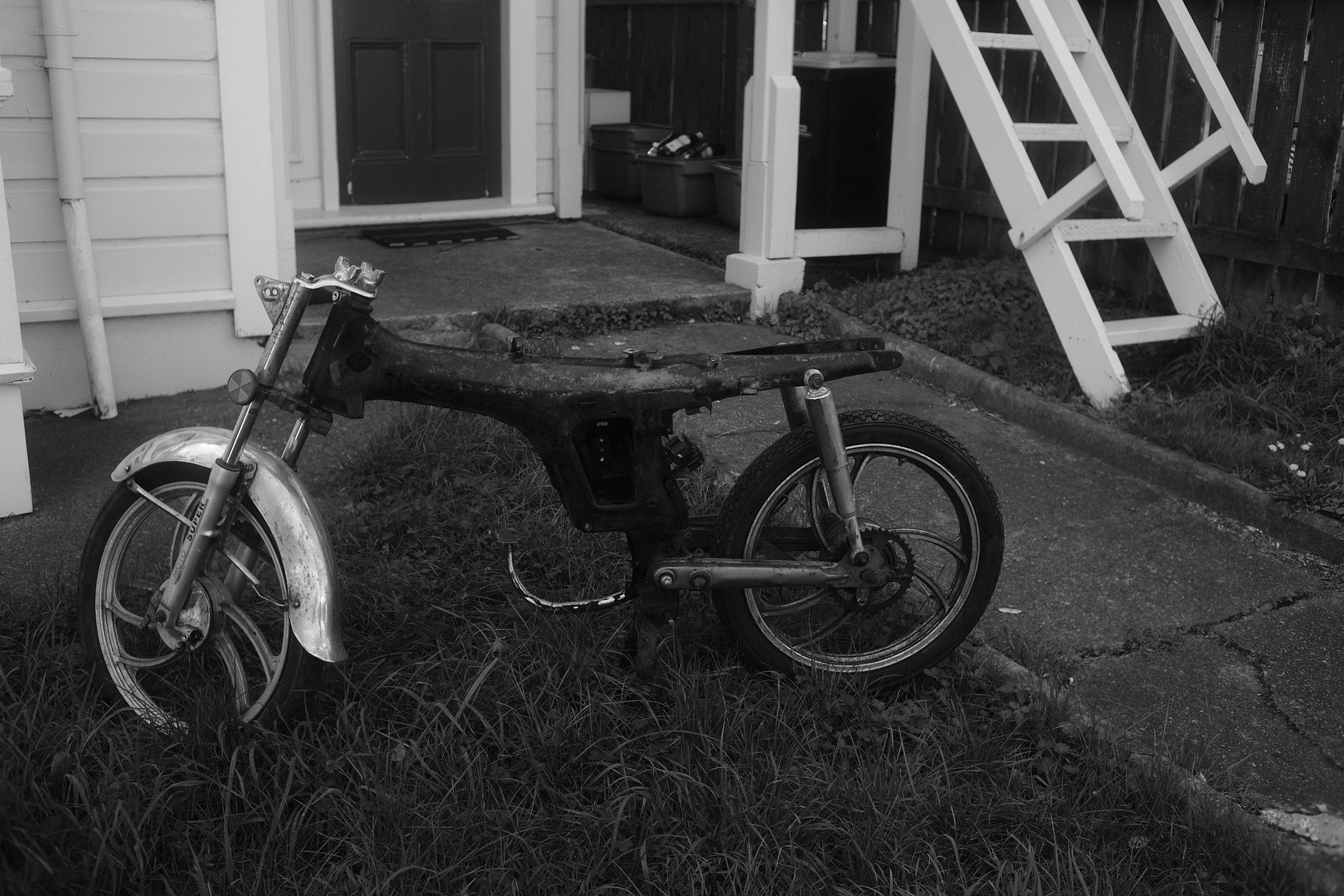 An empty frame of a motorbike sits in the front of someones yard.